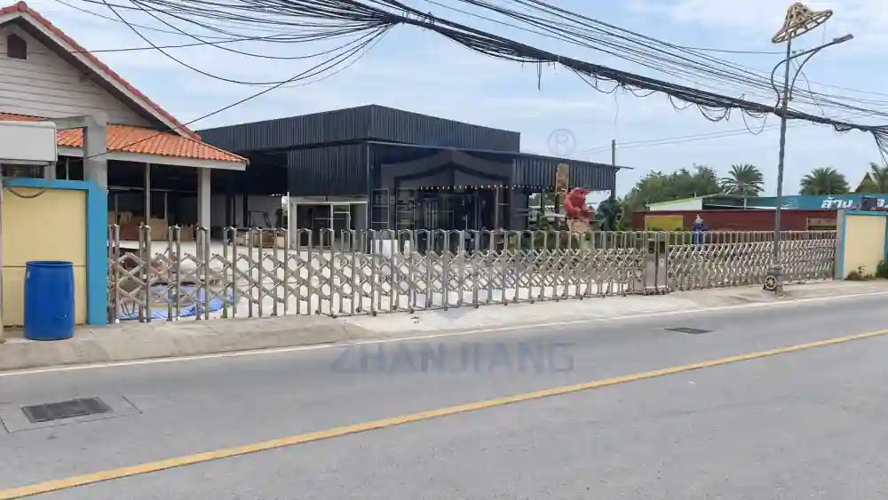 Silver stainless steel double-opening retractable gates across a roadside property entrance in Thailand